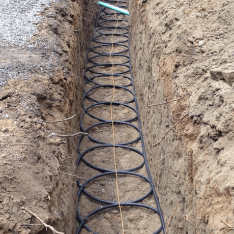 A coiled geothermal ground loop set into a narrow trench in Pacific Northwest soil.